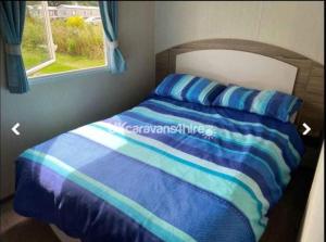 a bed with blue and white sheets and a window at Caravan Primrose Valley WW in Hunmanby