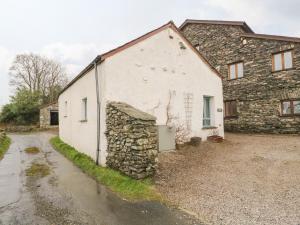 a white building with a stone wall next to a driveway at Eller Riggs Cottage in Ulverston