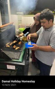 a man and a woman cooking food on a grill at Damai Holiday Homestay in Melaka