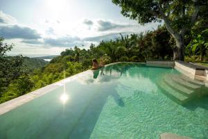 a woman sitting on the edge of a swimming pool at Tanah Damai Hotel in Nusa Penida