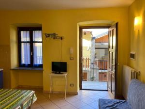 a yellow room with a television and a door to a balcony at Residenza Graziella in Bobbio Pellice