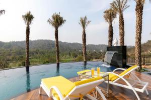 een zwembad met stoelen en palmbomen bij StayVista at Brickwood Hill with Outdoor Infinity Pool & Jacuzzi in Chandīgarh