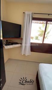 a room with a tv and a window with a curtain at Chalé com piscina privada vista mar-Zumbi-RN in Rio do Fogo