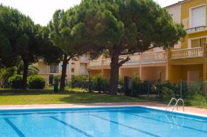 a swimming pool in front of a building with trees at Aptos. Comte D´Empuries in Empuriabrava