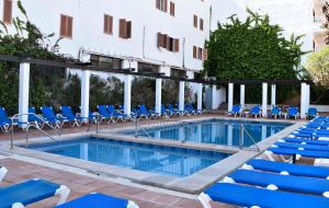 une piscine avec des chaises bleues et un bâtiment dans l'établissement Apartamentos Arcos Playa, à S'illot