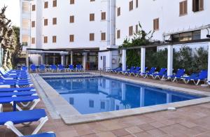 une piscine avec des chaises longues bleues et un bâtiment dans l'établissement Apartamentos Arcos Playa, à S'illot