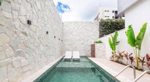 a swimming pool in front of a stone wall with two chairs at Flat Encantador Bauten Cabo Branco in João Pessoa