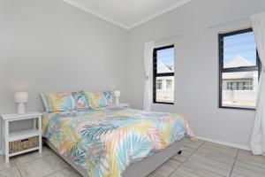 a bedroom with a bed with a colorful bedspread and two windows at Cheerful Cottage on Britannia Beach, West Coast in Britannia Bay