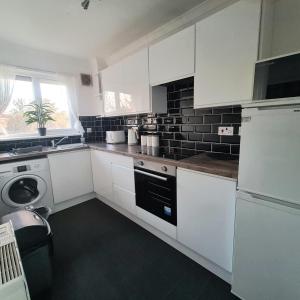a kitchen with white cabinets and a sink and a dishwasher at Levenhowe Holiday Apartment in Balloch