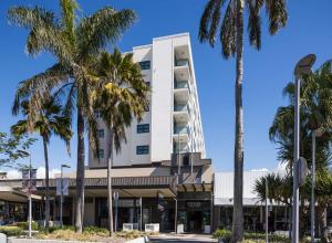 a tall white building with palm trees in front of it at Rydges Mackay Suites in Mackay