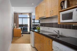 a kitchen with a sink, stove, microwave and refrigerator at Rydges Mackay Suites in Mackay