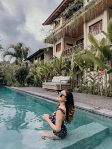 a woman sitting on the edge of a swimming pool at Jati Cottage in Ubud