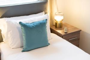 Cama con almohada azul y mesa con lámpara en Spacious 3 Bed - Smart TVs - Great for Work Stays, en Swansea
