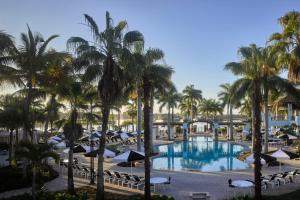 パームビーチ・ガーデンズにあるPGA National Resortのヤシの木と傘が備わるプールの景色を望めます。