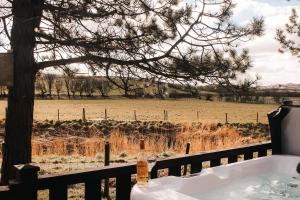 eine Badewanne neben einem Zaun mit einem Feld in der Unterkunft Keer Side Lodge, Luxury lodge with private hot tub at Pine Lake Resort in Carnforth