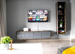 een woonkamer met een flatscreen-tv aan de muur bij “Pop Inn” modern apartment in heart of Bryanston in Johannesburg