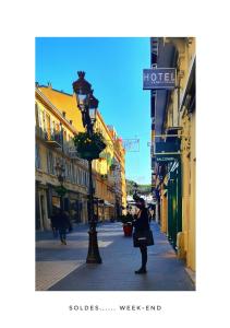 une femme debout dans une rue avec un pôle lumineux dans l'établissement Le Petit Trianon et le Charme des Suites, à Nice