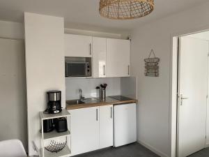 uma pequena cozinha com armários brancos e um micro-ondas em Cabourg T2 cosy avec accès direct plage em Cabourg
