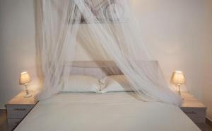 a white bed with white curtains and two lamps at Efi Apartments in Agios Gordios