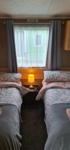 two beds in a room with a window and a lamp at Carmels Caravan Borwick Lakes in Carnforth