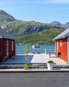 a dock with two red buildings and a boat in the water at Lofoten Cabins - Kåkern in Ramberg