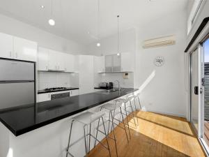 a white kitchen with a black counter top and stools at Anderson Central Torquay 36 in Torquay