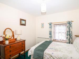 a bedroom with a bed and a dresser and a window at Swift Cottage in Mawgan in Meneage