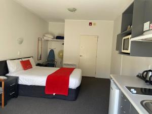 Habitación pequeña con cama con manta roja en Ascot Motor Lodge en Wellington