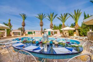 a table with chairs and a pool with palm trees at Can Comaro in Alcudia