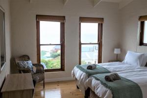 a bedroom with two beds and a table and windows at Boulders Beach House in Simonʼs Town