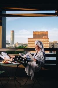 uma mulher sentada numa varanda a ler um jornal em Hallmark Hotel by BON Hotels em Joanesburgo