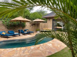 a pool with chairs and umbrellas in a yard at Sunbird Cottage in Usa River