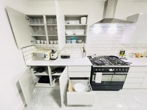 Leytonstone House - SleepyLodge في لندن: مطبخ بدولاب بيضاء وموقد
