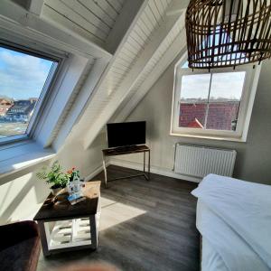 a attic room with a bed and a tv and two windows at HOTEL DÜNENLÄUFER Carolinensiel in Carolinensiel