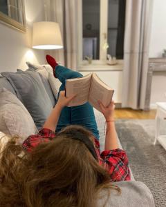 Una chica acostada en un sofá leyendo un libro en EL GUSTO HOMES Town, en Sopron