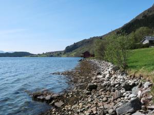 une rive rocheuse d'un lac avec une maison en arrière-plan dans l'établissement Holiday Home Idun - FJS131 by Interhome, à Hyllestad
