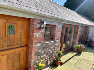 a brick building with a wooden door and flowers at The Old Coach House in Pen-pergwm