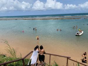 Dos mujeres mirando a la gente en el agua en una playa en Nannai Residence Flat - Muro Alto, en Porto de Galinhas