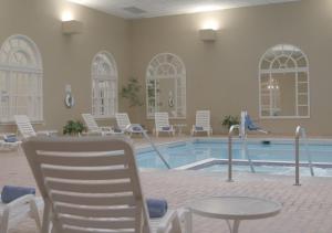 una piscina con sillas blancas, una mesa y una piscina en The Queensbury Hotel en Glens Falls