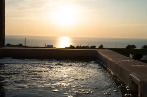 a pool of water with the sun in the background at The Lighthouse Sunset View Suites in Akrotiri