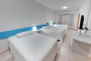 a white room with two beds and a tv at Amazon Plaza Hotel in Cuiabá