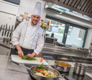 - un chef découpant des légumes sur un plateau de découpe dans une cuisine dans l'établissement Gasthof Rabenstein, à Sarentino