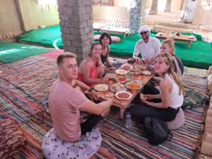 a group of people sitting around a table eating food at White Desert Soul Safari Camp Desert Experience in Mandīshah +114 photos