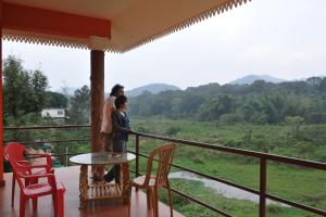Dos personas de pie en un balcón con una mesa y sillas. en Konark Homestay, en Thekkady