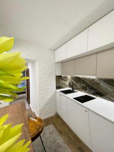 una cocina con armarios blancos, una mesa y una flor amarilla en Colorway Apartment en Belgrado