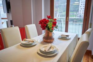 una mesa con platos y un jarrón con flores rojas en Apartamento BIO Exclusivo con mirador en Bilbao y aparcamiento público gratuito, en Bilbao