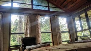 Schlafzimmer mit großen Fenstern, einem Bett und einem Stuhl in der Unterkunft Jungle Jive Tree House in Munnar