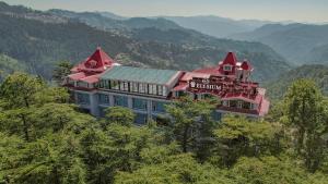 un grand bâtiment au sommet d'une colline plantée d'arbres dans l'établissement WelcomHeritage Elysium Resort & Spa, à Shimla