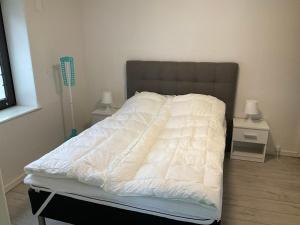 a bed with a white comforter and two night stands at Strandhytten in Hvide Sande