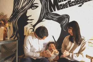 Um homem e uma mulher a segurar um bebé em frente a um mural. em Camellia Complex em Inawashiro